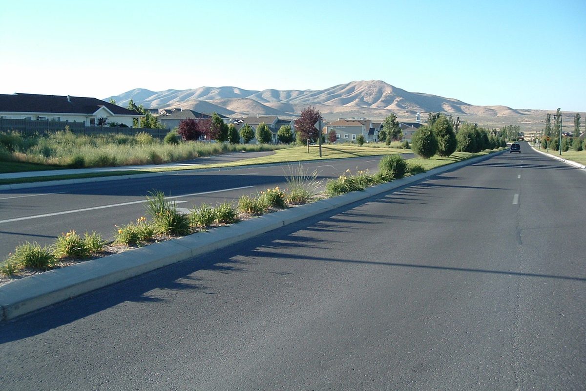 Pony Express Parkway in Eagle Mountain, a wide divided road with a planted median, houses on the left and bare brown hills ahead under a clear sky
