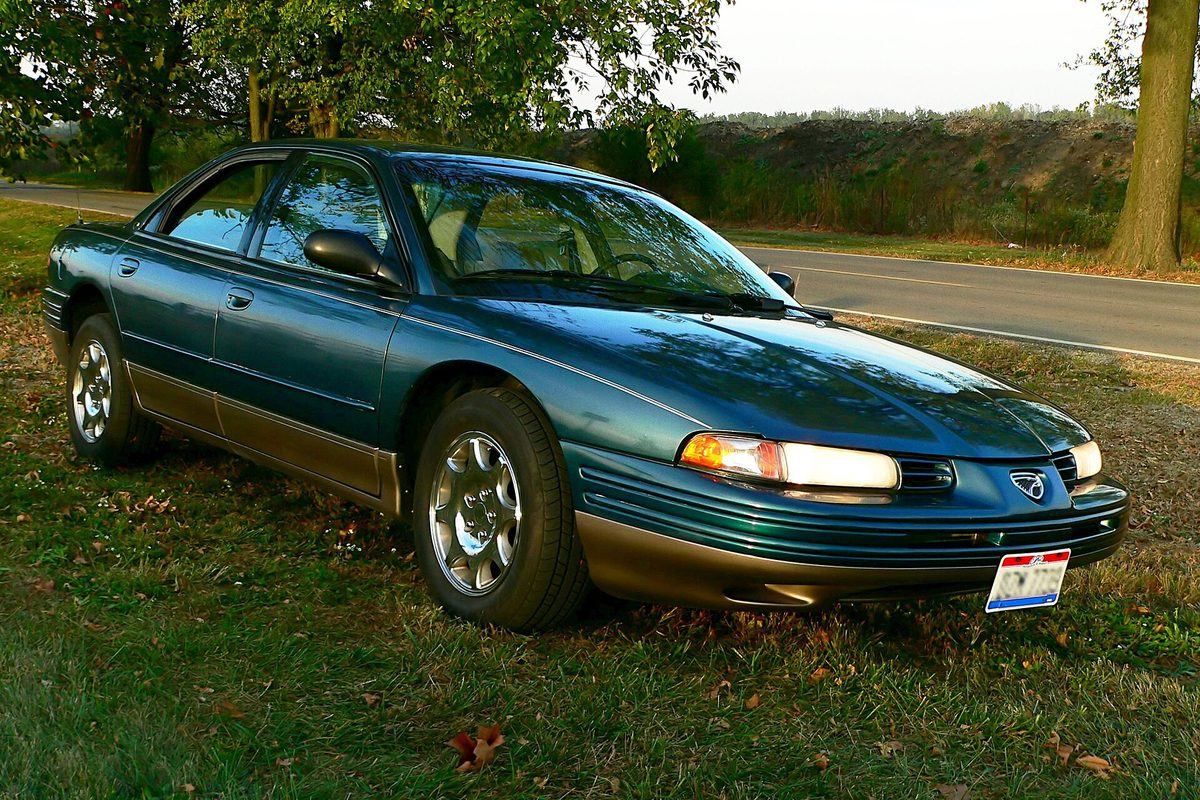 A dark green Eagle Vision ESi sedan with gold-toned lower trim, parked on grass beside a country road