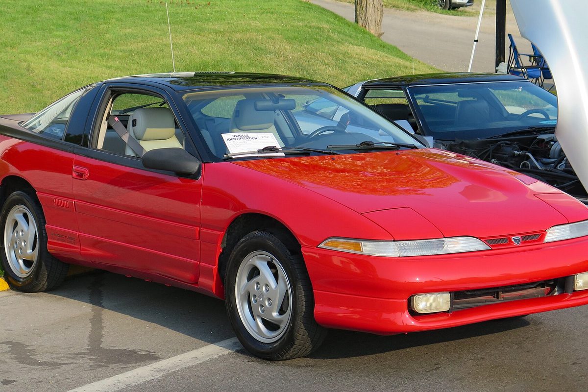 A red 1991 Eagle Talon TSi AWD hatchback coupe with pop-up headlights, parked at an outdoor car show, seen from the front right