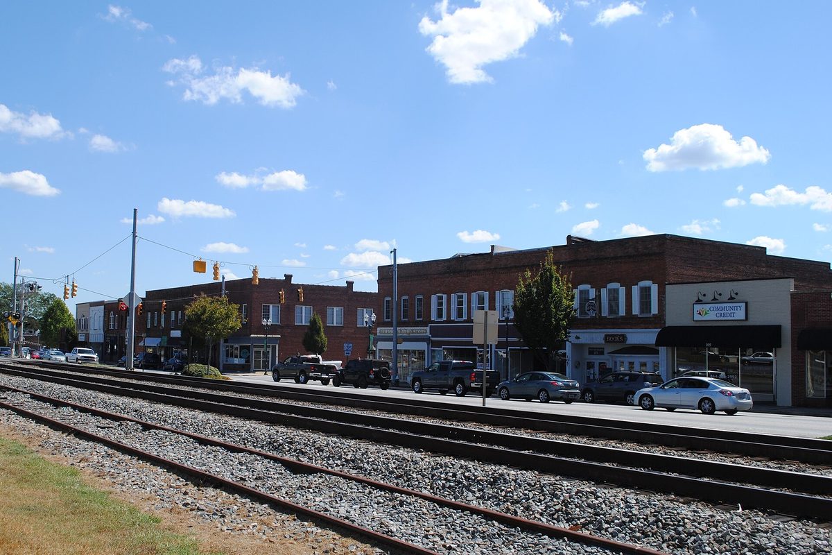 Railroad tracks running past a row of two-story brick storefronts and parked pickups in downtown Easley under a blue sky