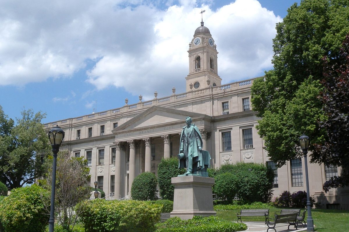 East Orange City Hall, a pale stone building with columns and a clock tower, behind a bronze statue of Abraham Lincoln on a stone pedestal