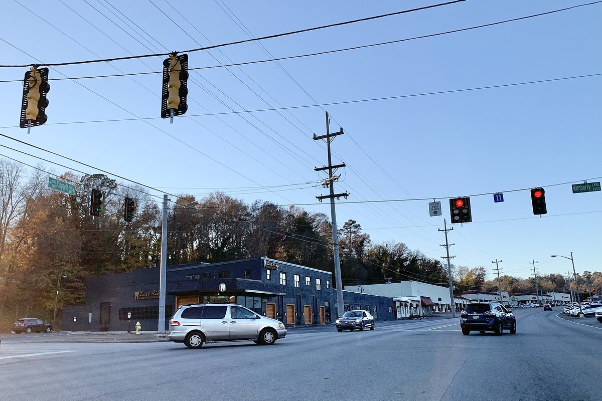 Traffic lights over Ringgold Road at Wimberly Lane in East Ridge, with a minivan turning past a dark-blue commercial building and autumn trees
