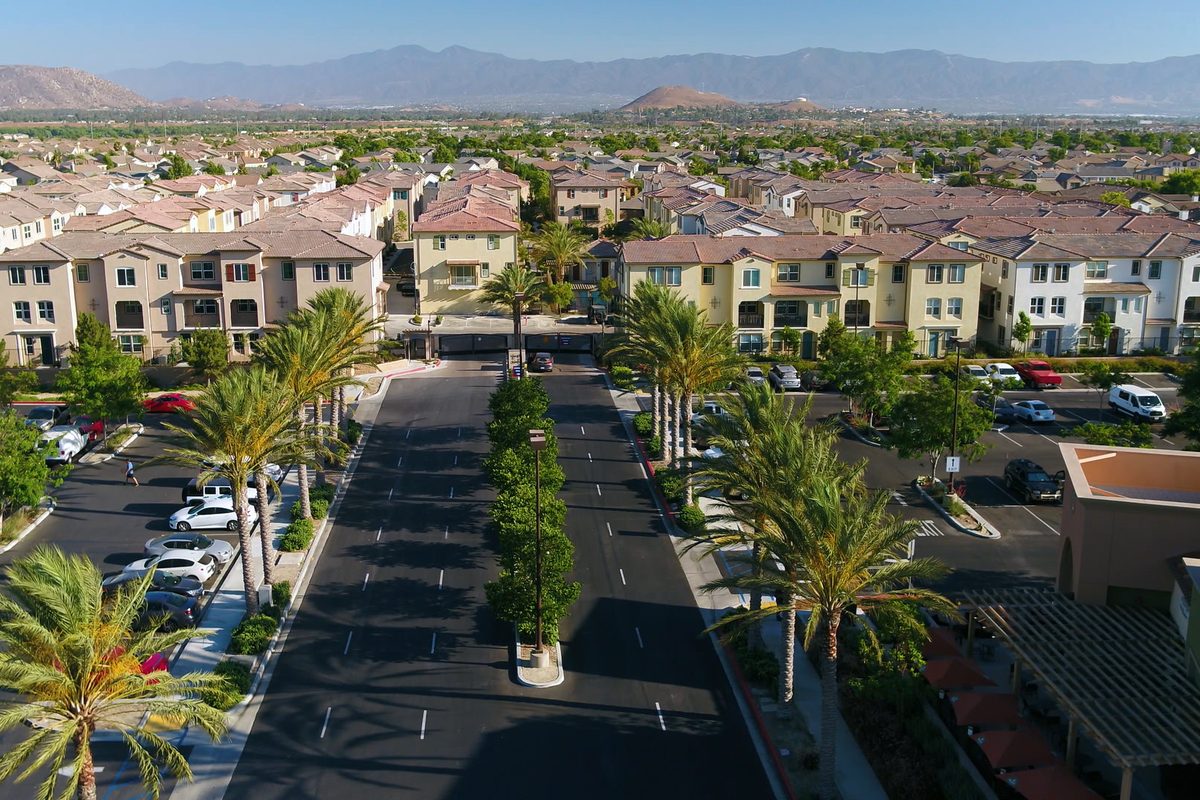 Two-story Eastvale townhomes with tile roofs along a palm-lined street with a planted median, mountains in the distance