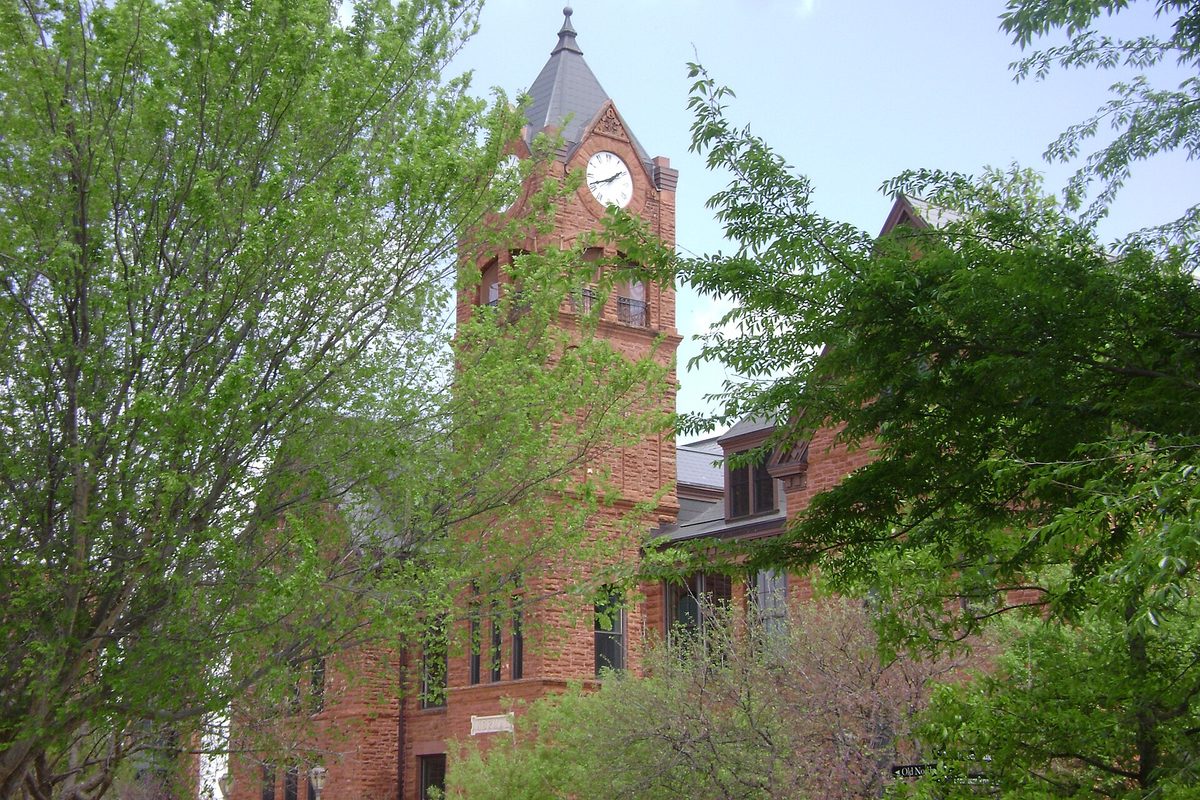 The red brick clock tower of Old North at the University of Central Oklahoma, half hidden behind leafy spring trees
