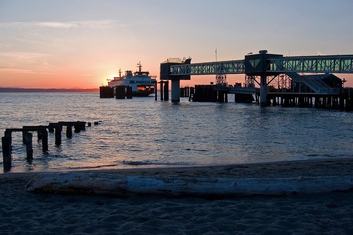 The Edmonds-Kingston ferry arriving at the Edmonds terminal at sunset, with old wooden pilings in the water and a driftwood log on the sand