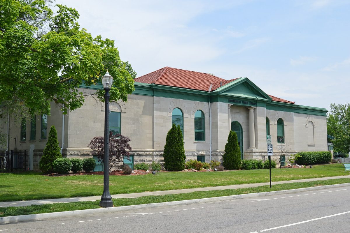 The Edwardsville Public Library, a pale stone Carnegie building with a red tile roof, arched windows and a lamp post out front