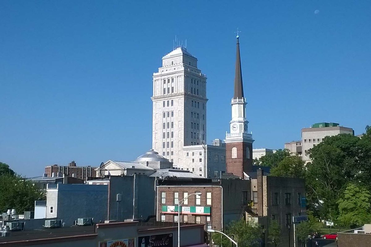 The tall white Union County Courthouse tower and a white church steeple rising above downtown Elizabeth rooftops under a blue sky