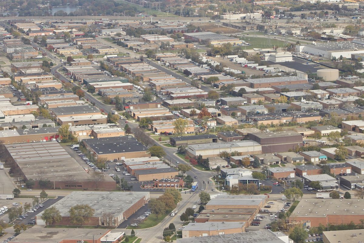 Aerial view of rows of low warehouse and factory roofs, parking lots and autumn trees in an Elk Grove Village industrial park