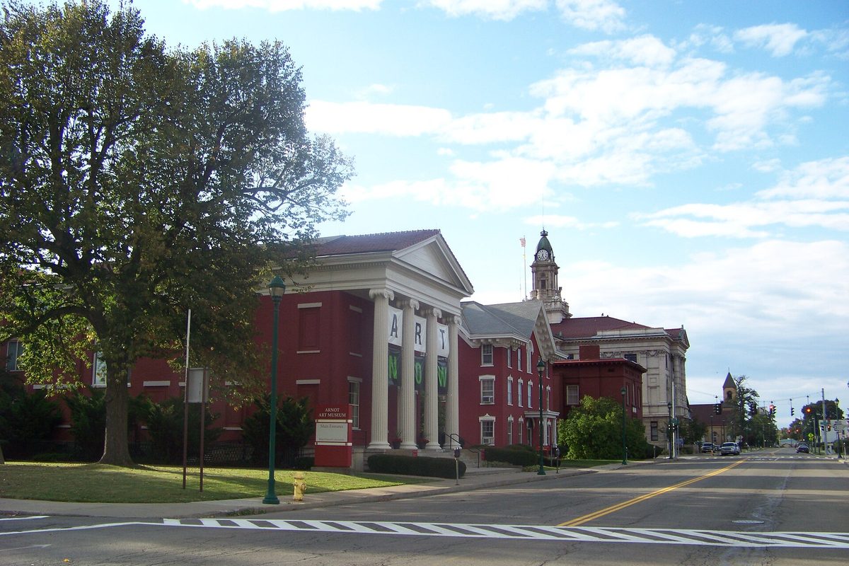 A red brick building with white columns and ART banners on Main Street in Elmira's Civic Historic District, with a clock tower rising behind it