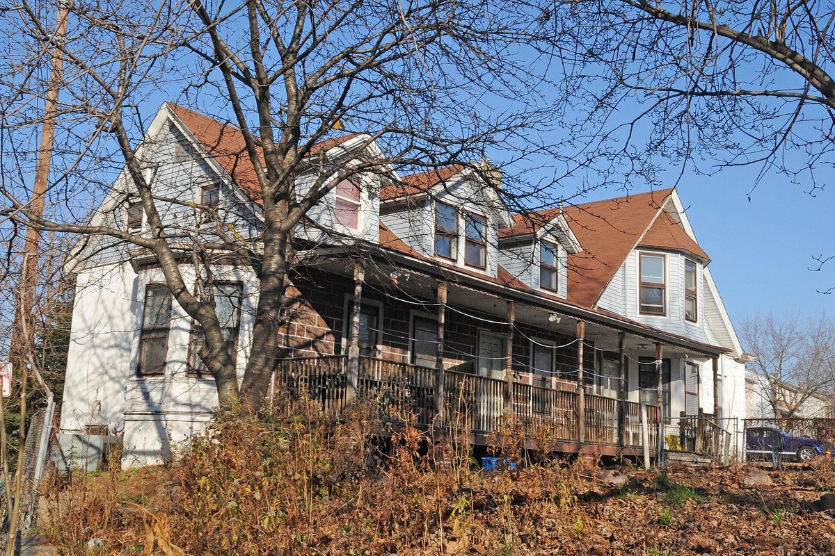 The Van Houten-Hillman House in Elmwood Park, a long white house with dormers, a red roof and a wide porch, seen through bare winter trees