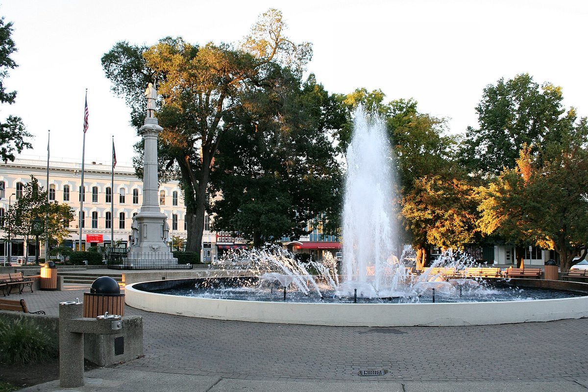 The fountain in Ely Park in downtown Elyria, with the Civil War memorial column, early autumn trees and a row of storefronts behind