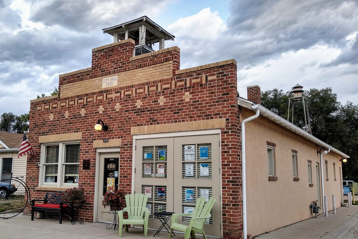 Erie's 1930 red brick former town hall with a white cupola on top, green Adirondack chairs by the door and an old water tower behind it