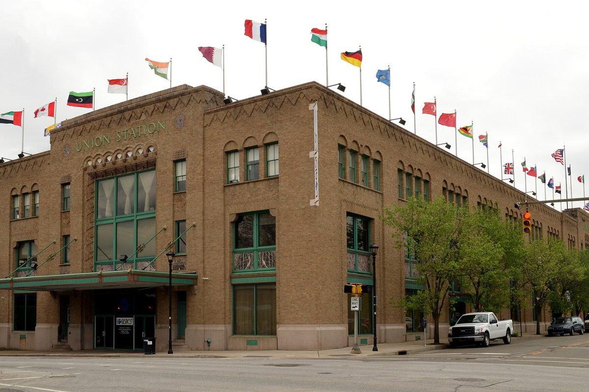 Erie's Union Station, a long tan brick building with arched windows and a row of national flags along its roofline, with a white pickup parked out front
