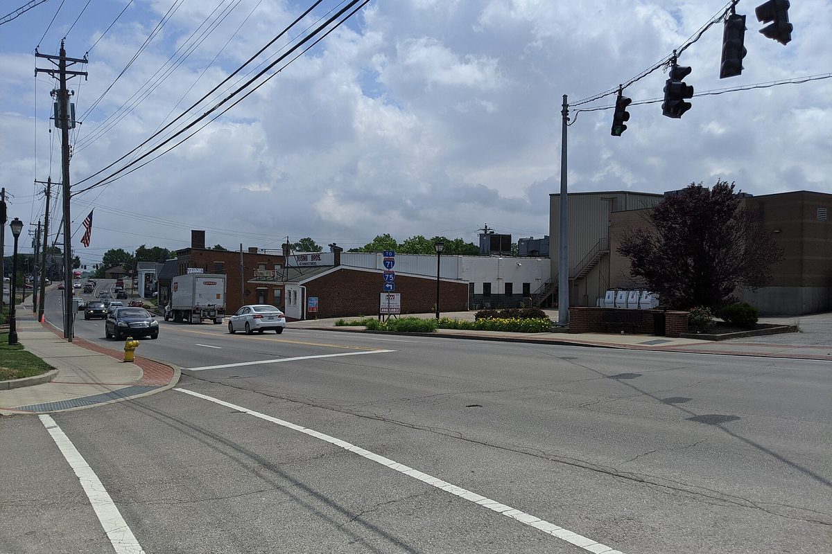 Dixie Highway through downtown Erlanger under a cloudy sky, with overhead traffic lights, a box truck and low brick buildings
