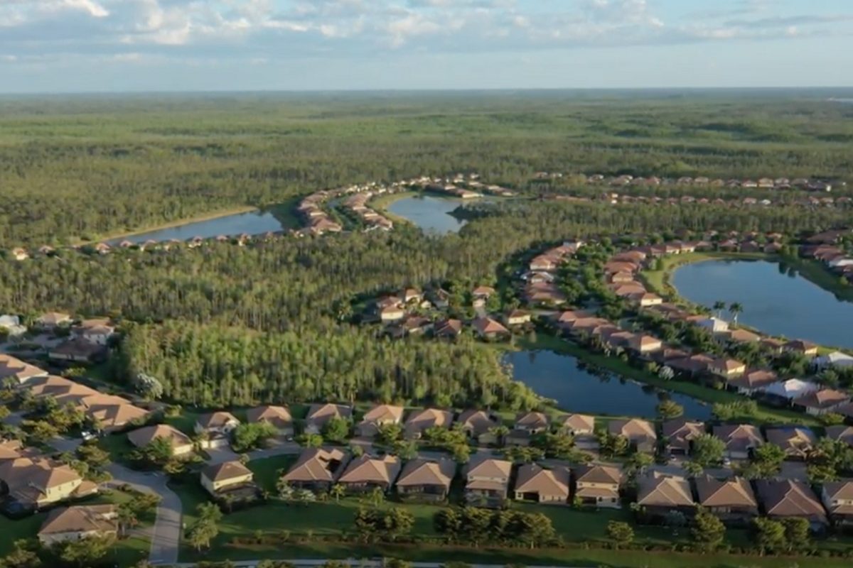 Aerial view of the Bella Terra neighborhood in Estero: rows of tile-roofed homes around lakes, with pine forest stretching to the horizon