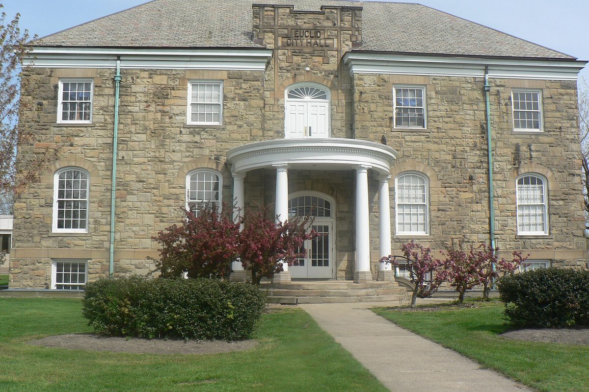 Euclid's old city hall, a two-story sandstone building with a rounded, columned entry porch, red-leafed shrubs and a front walk across the lawn