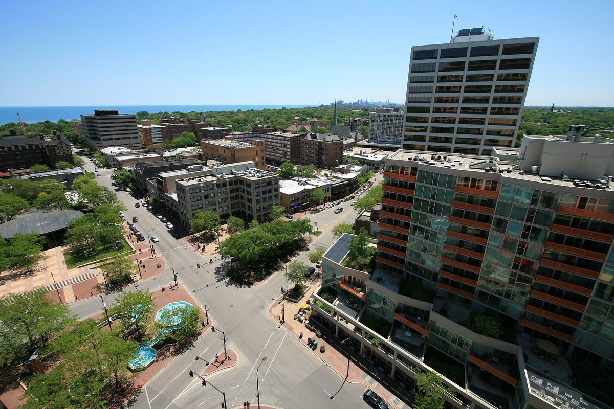 High view over downtown Evanston and Fountain Square, with tall buildings in the foreground, Lake Michigan on the left and the Chicago skyline on the far horizon