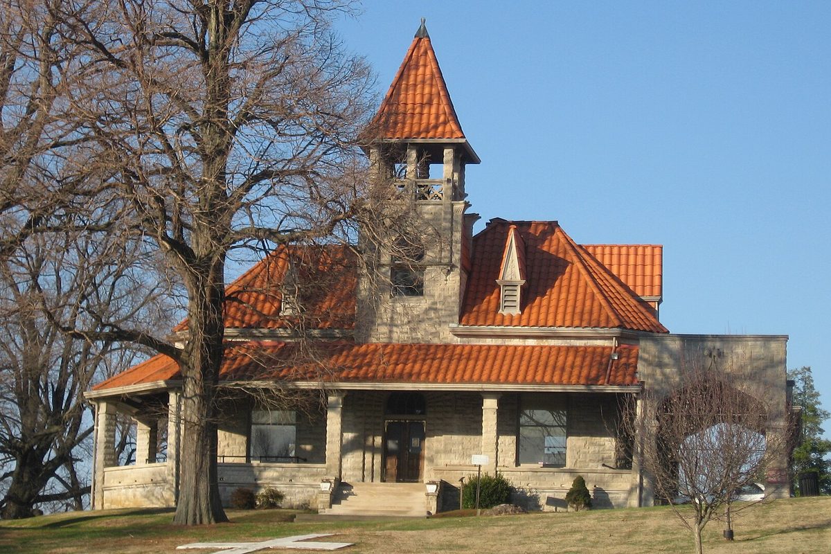 The stone administration building at Oak Hill Cemetery in Evansville, with an orange tile roof and a pointed bell tower, framed by bare trees