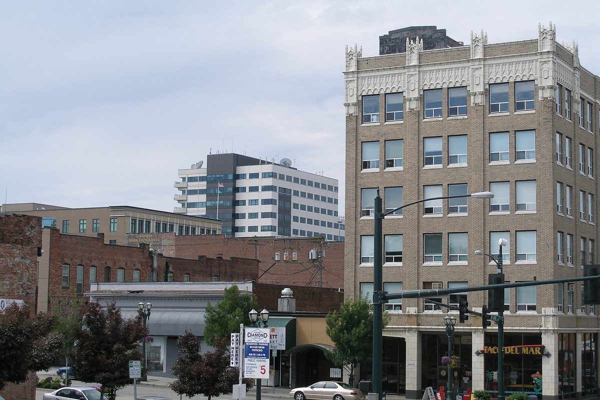 A downtown Everett street with an ornate tan brick building on the corner, older brick storefronts and an office tower behind