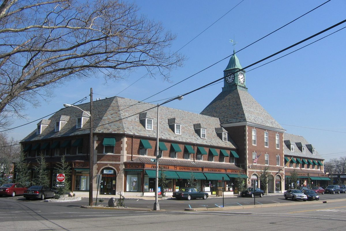 Radburn Plaza in Fair Lawn, a brick shopping building with a slate roof, green awnings and a clock tower, under a clear sky