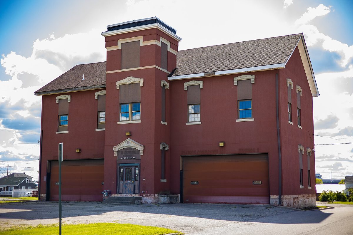 Fairborn's historic red brick fire station, a two-story building with a short tower, arched trim and two large garage doors, under a blue sky with clouds