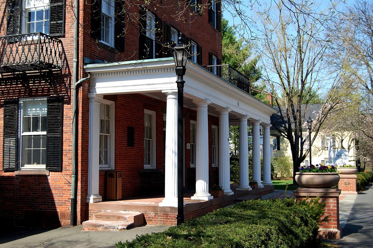 The brick main building at Miss Porter's School in Farmington, with a white-columned porch, black shutters and a lamppost in spring
