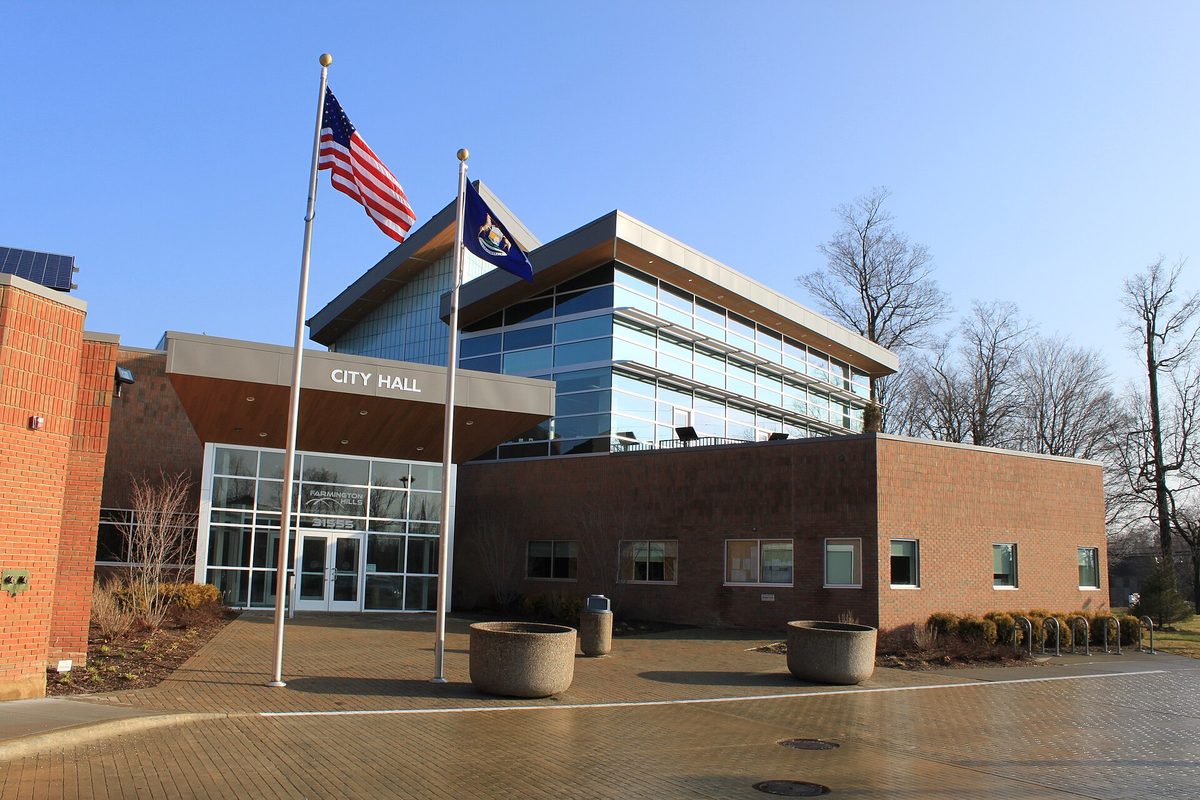 Farmington Hills City Hall, a brick and glass building with City Hall lettered over the entrance and U.S. and Michigan flags out front