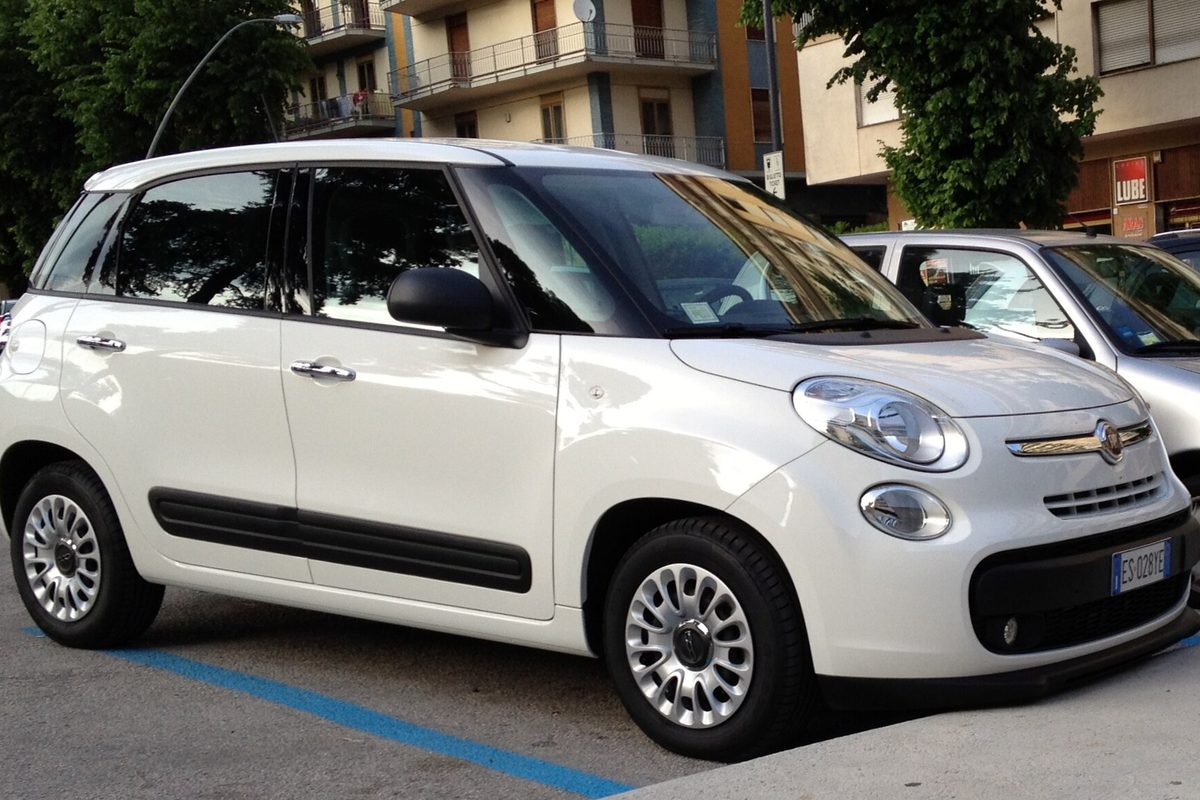 A white Fiat 500L wagon with silver wheel covers and black side trim, parked in a lot beside apartment buildings