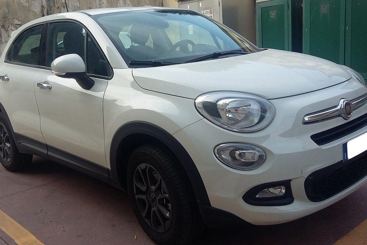 A white Fiat 500X crossover with dark alloy wheels and chrome front trim, seen from the front corner on a paved lot