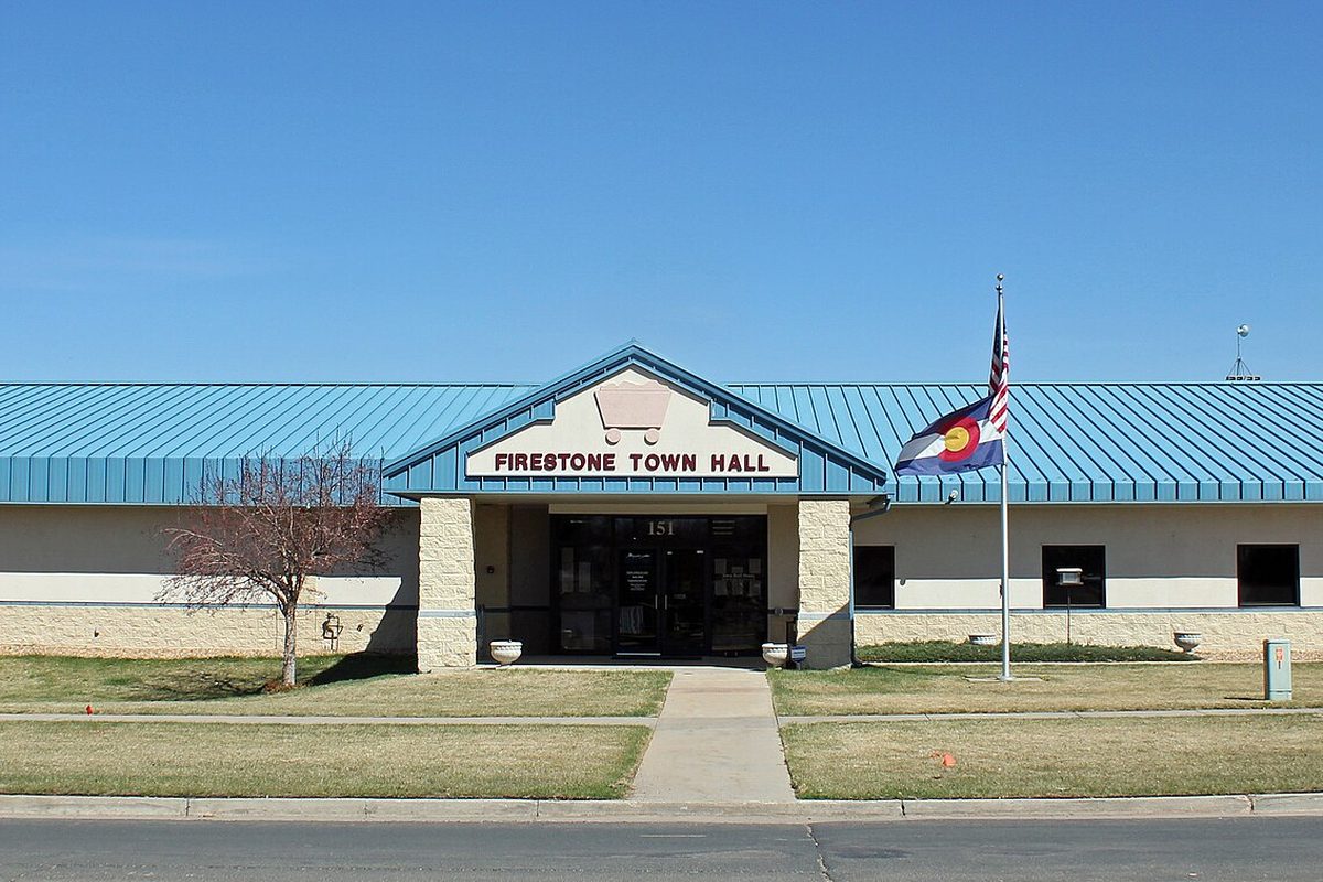 The single-story former Firestone Town Hall at 151 Grant Avenue, with a teal metal roof, a stone-trimmed entrance and a Colorado flag flying on the lawn