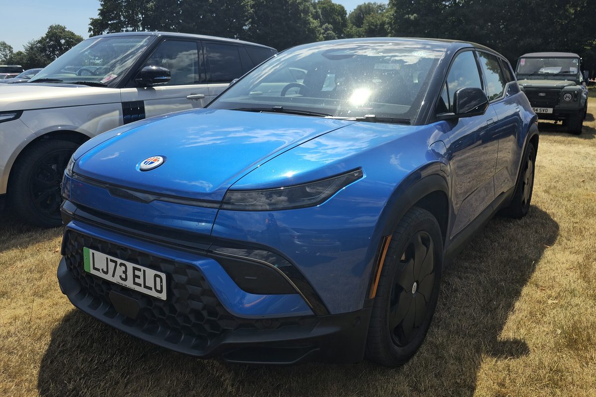 A bright blue Fisker Ocean electric SUV parked on dry grass at an outdoor show, with other SUVs behind it