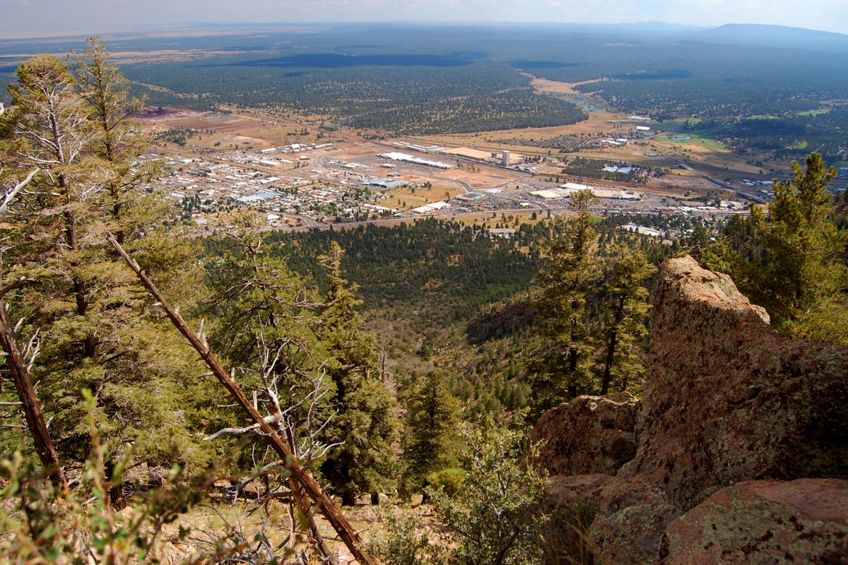 Flagstaff spread across a valley below pine forest and red rock, seen from the Mount Elden lookout