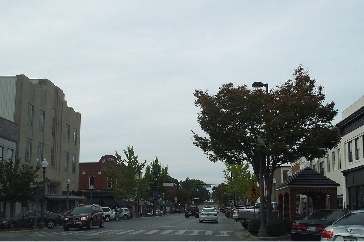 A street in the Downtown Florence Historic District on an overcast day, older brick and stone buildings on both sides, a leafy tree and parked cars along the curb