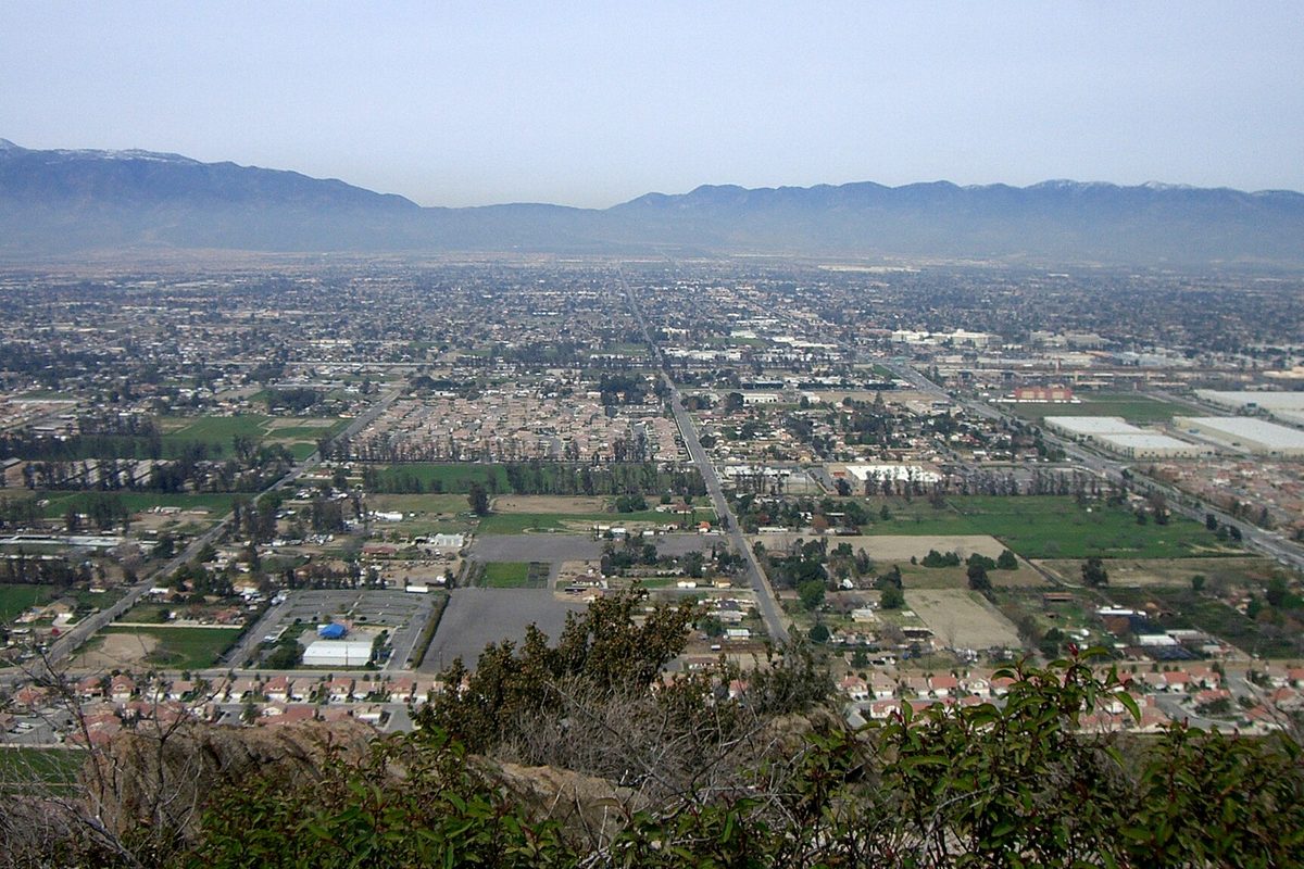 Fontana seen from a brushy hilltop, neighborhoods, fields and a long straight road stretching across the valley to the mountains