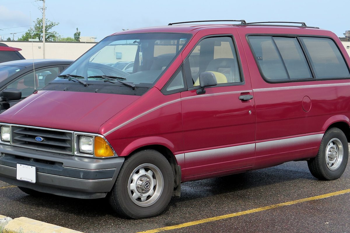A dark red 1991 Ford Aerostar XL minivan with gray lower trim and roof rails, parked on wet pavement by a curb