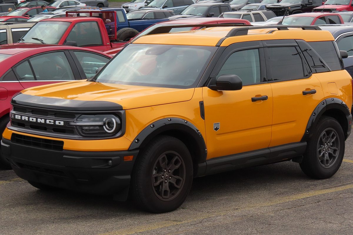 An orange 2022 Ford Bronco Sport Big Bend with black fender flares, parked in a dealer lot crowded with cars and pickups