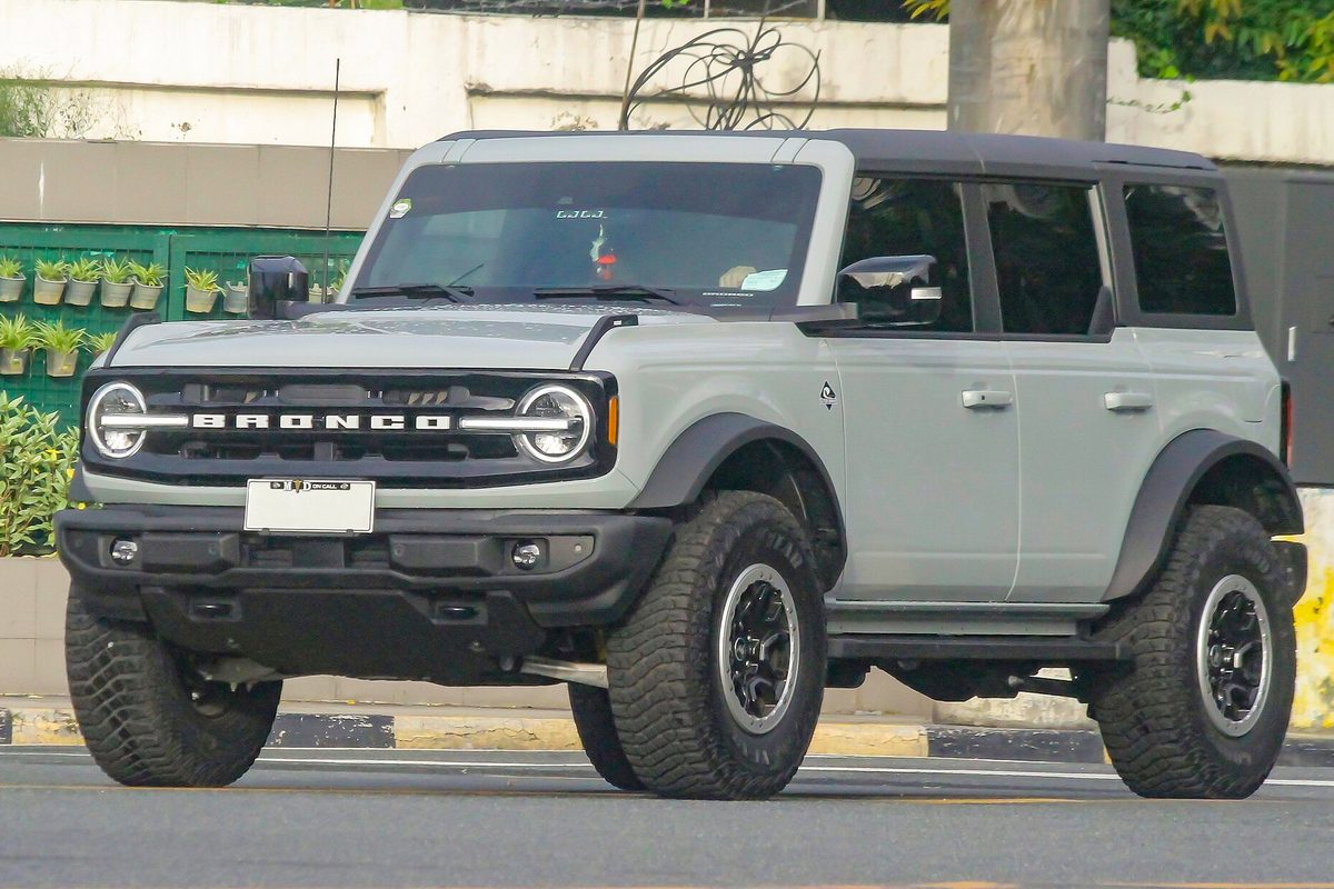 A Cactus Gray four-door Ford Bronco with black fender flares and large off-road tires on a city street