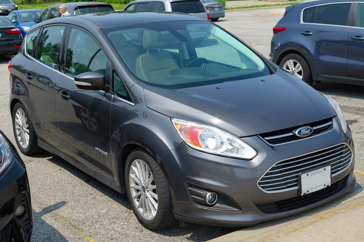 A dark gray 2015 Ford C-Max Hybrid SEL hatchback with a chrome grille, parked at a curb in a parking lot on a sunny day