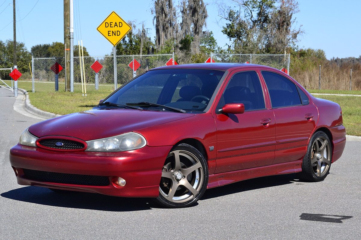 A red 1998 Ford Contour SVT sedan with five-spoke wheels on an empty road, a yellow Dead End sign behind it