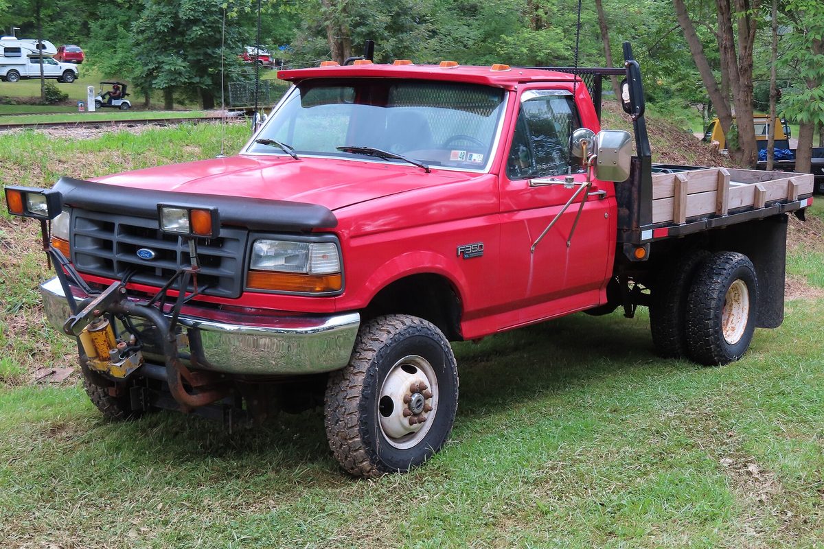 A red 1997 Ford F-350 dually regular cab with a flatbed and a plow mount and plow lights on the front, parked on grass