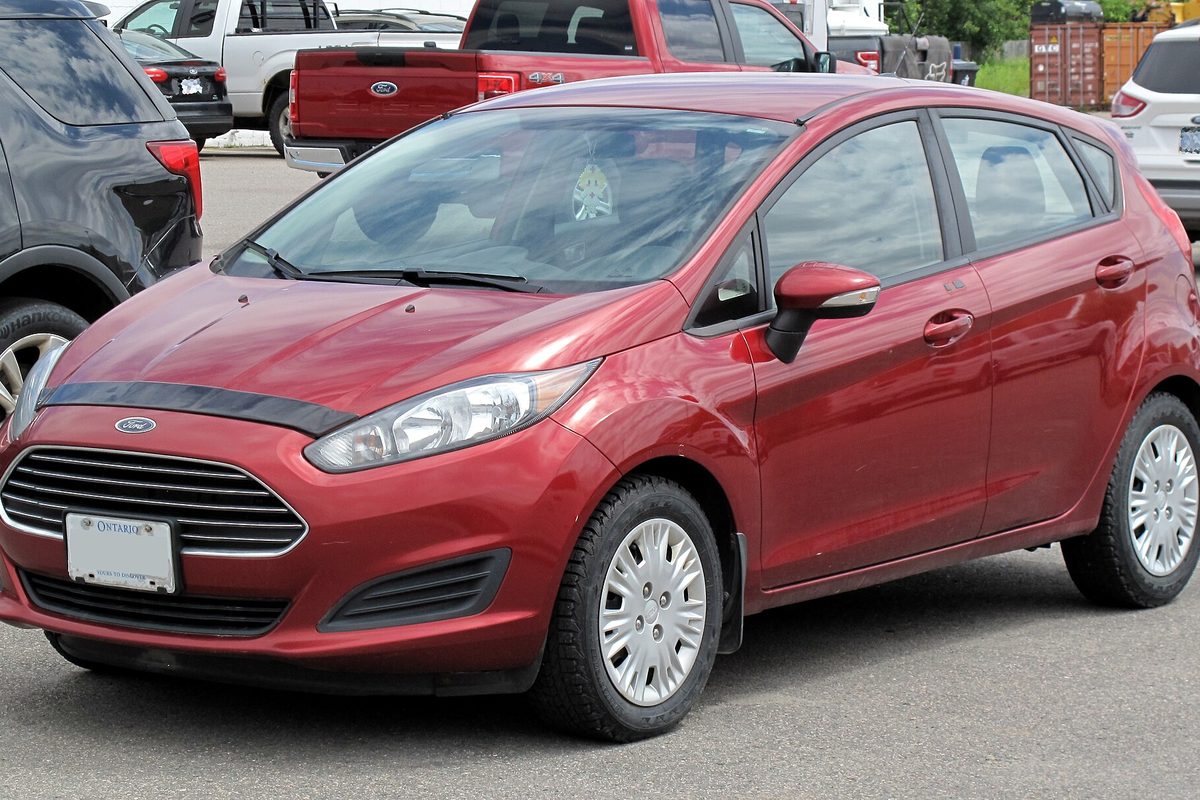 A red 2014 Ford Fiesta SE hatchback with silver wheel covers, parked in a lot in front of a red Ford pickup