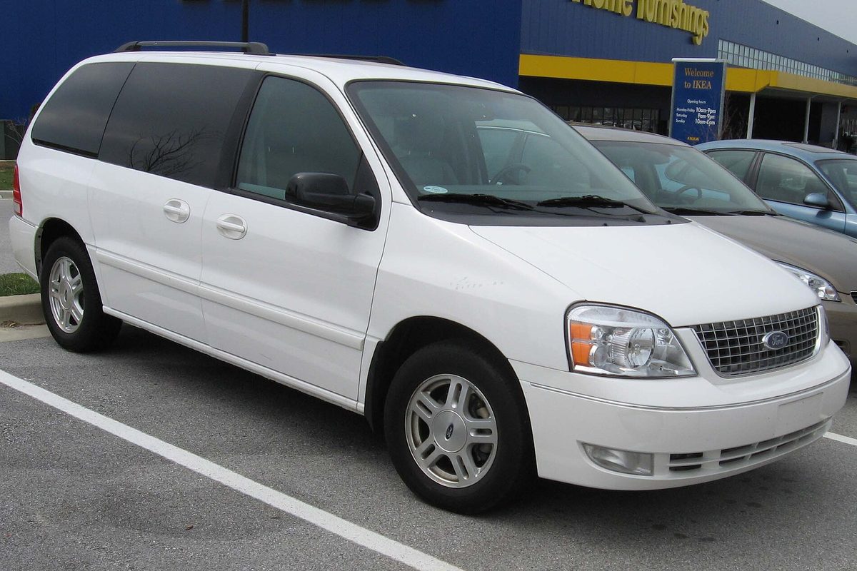 A white Ford Freestar minivan in a store parking lot, with a blue and yellow warehouse building behind it