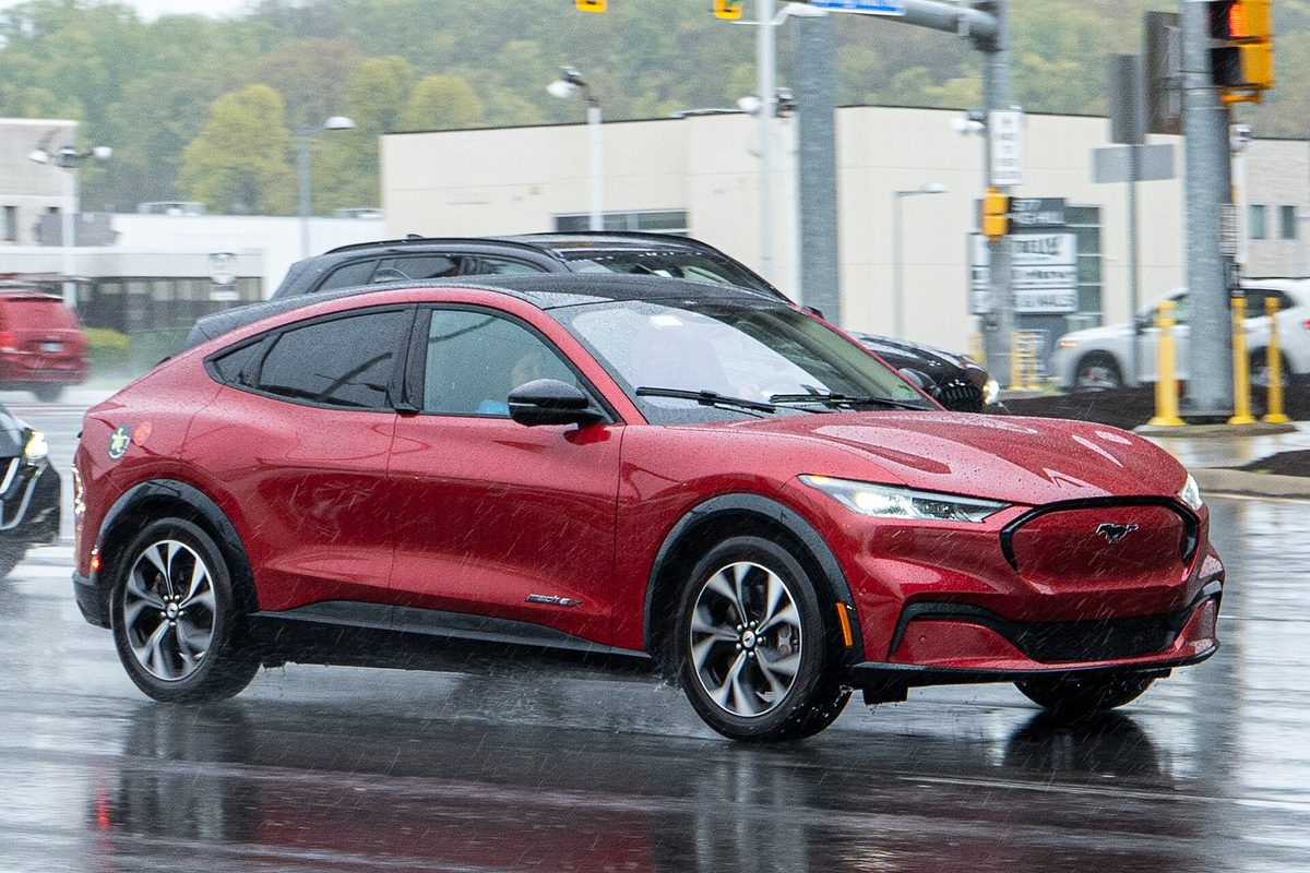 A red Ford Mustang Mach-E driving through heavy rain on a wet road near a traffic light