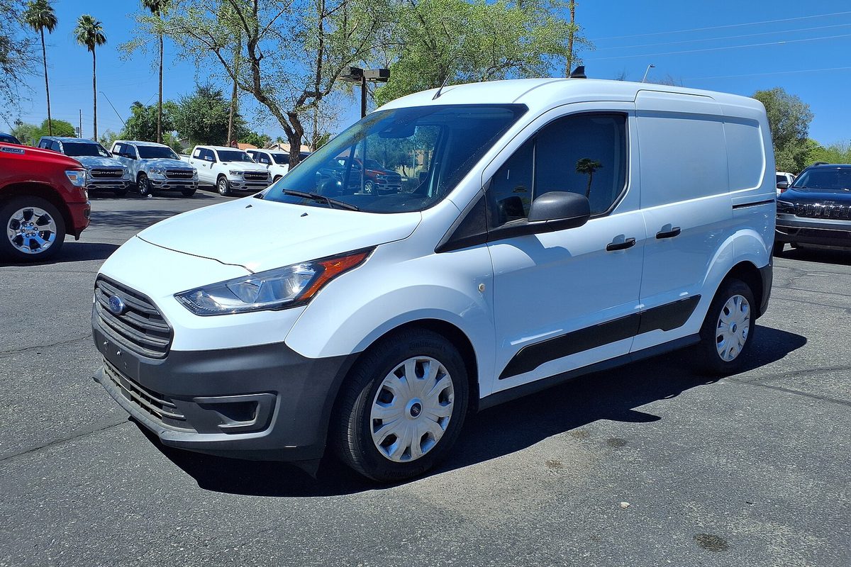A white 2022 Ford Transit Connect cargo van with steel wheels and plain hubcaps, parked on a sunny lot with palm trees behind it