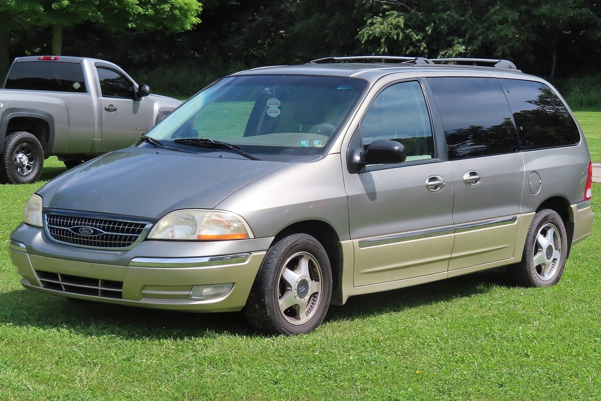A 1999 Ford Windstar SEL, gray-khaki over a champagne lower band, parked on grass with a silver pickup behind it