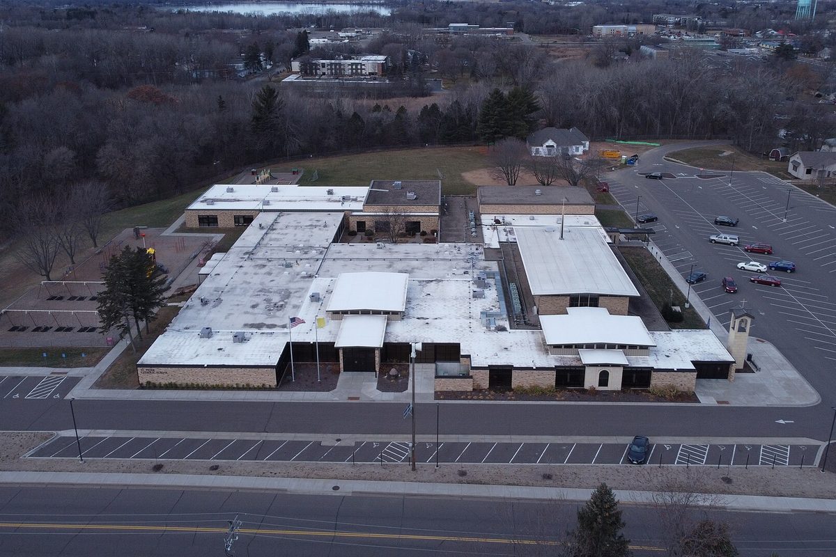 Aerial view of St. Peter's Catholic Church in Forest Lake, a wide flat-roofed building with a small bell tower and parking lots, among bare trees at dusk