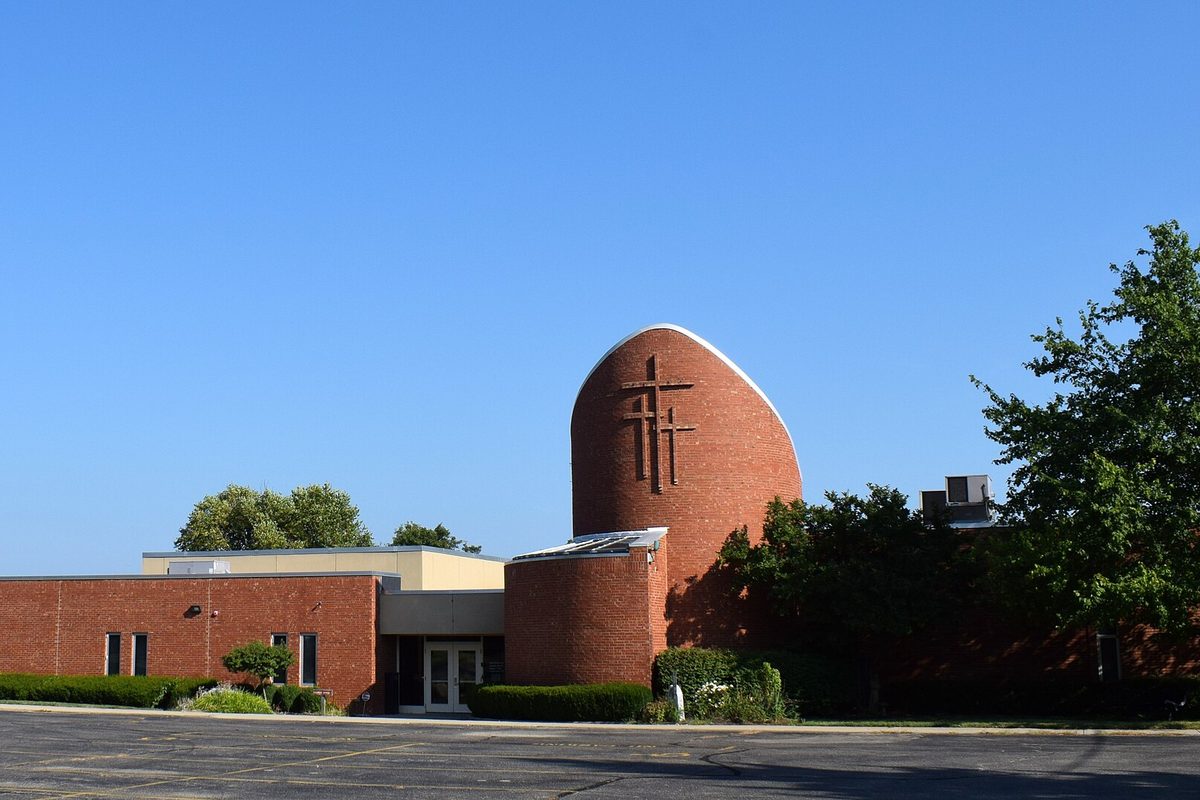 Saint Matthias the Apostle Church, a low brick building with a tall rounded brick tower bearing two crosses, across an empty parking lot under a clear blue sky