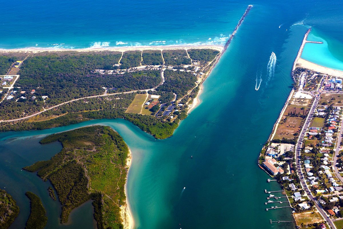 Aerial view of Fort Pierce Inlet, with turquoise water running between a wooded barrier island and a strip of waterfront homes out to the Atlantic