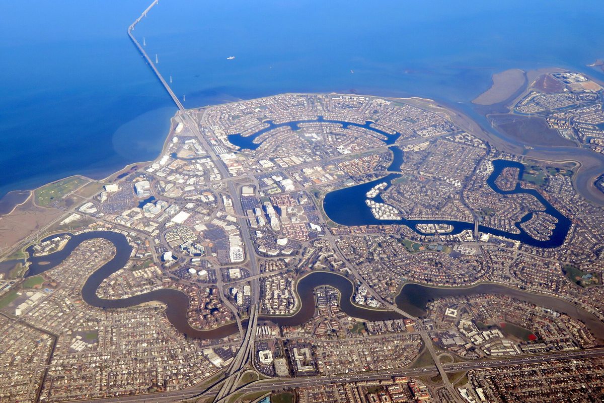 Aerial view of Foster City's winding lagoons and neighborhoods on the edge of San Francisco Bay, with a long bridge running out across the water