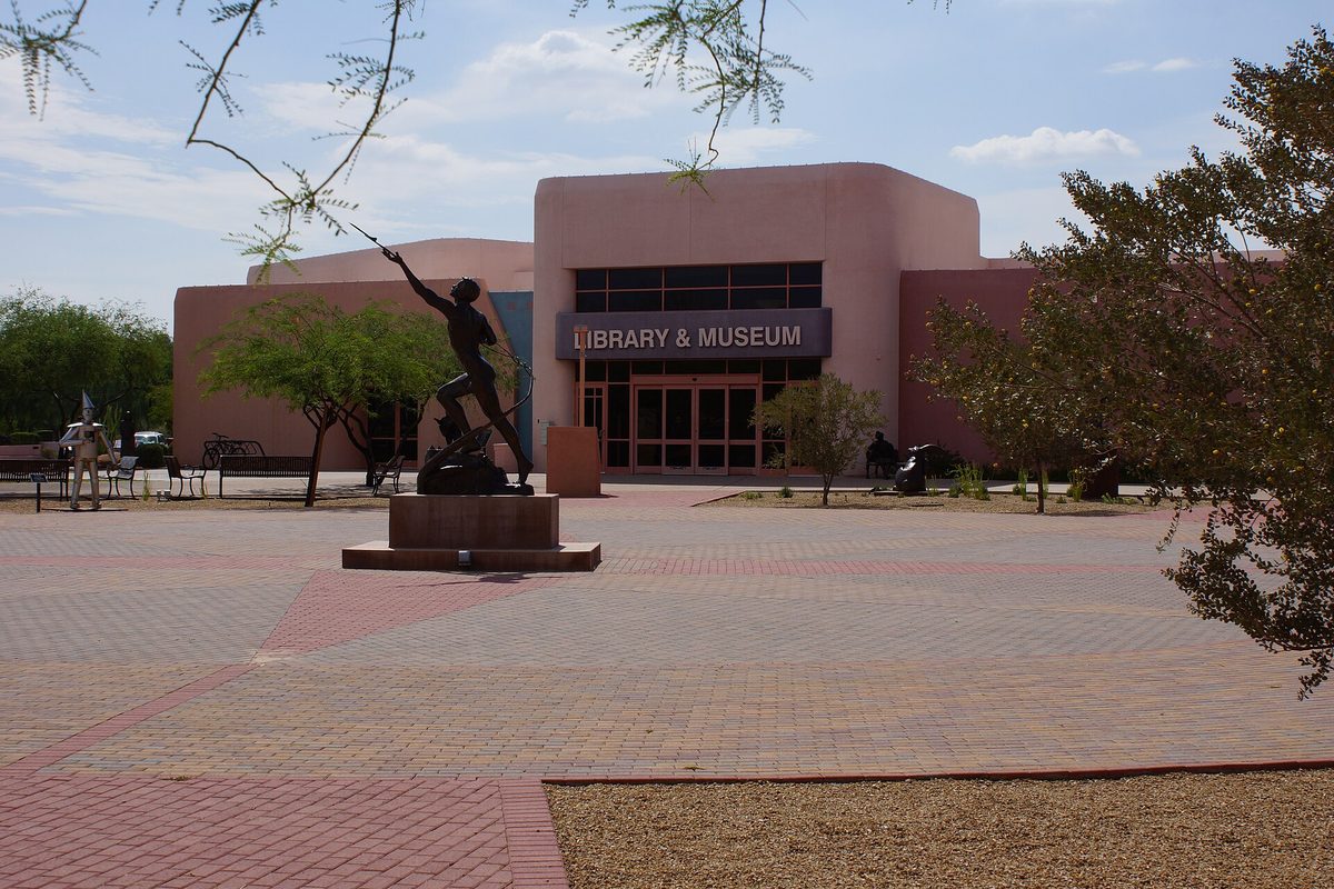 The pink stucco Fountain Hills Library and Museum behind a brick plaza with a bronze figure on a pedestal